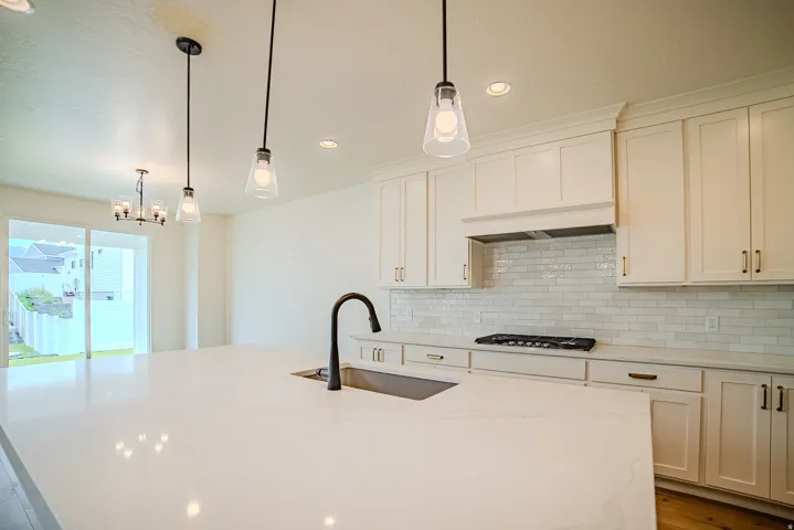 Spacious kitchen featuring a large island with an undermount sink and matte black faucet, white shaker cabinetry, white subway tile backsplash, and a gas range