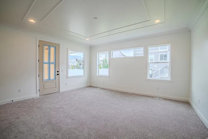 Bright room featuring a tray ceiling with recessed lighting, multiple windows, and light-toned carpet