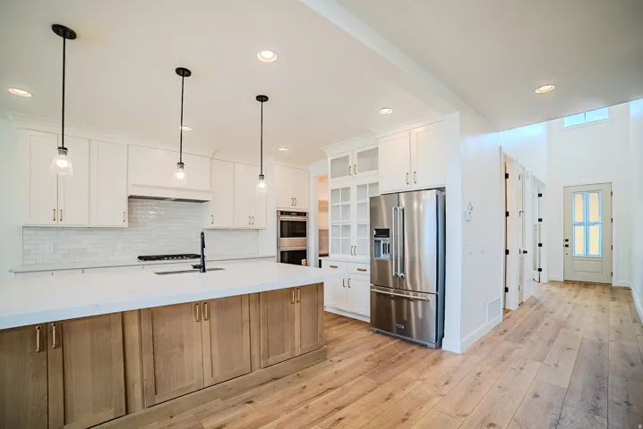 Gourmet kitchen with a large two-tone island, white perimeter cabinetry, stainless steel appliances, and wood-finish flooring