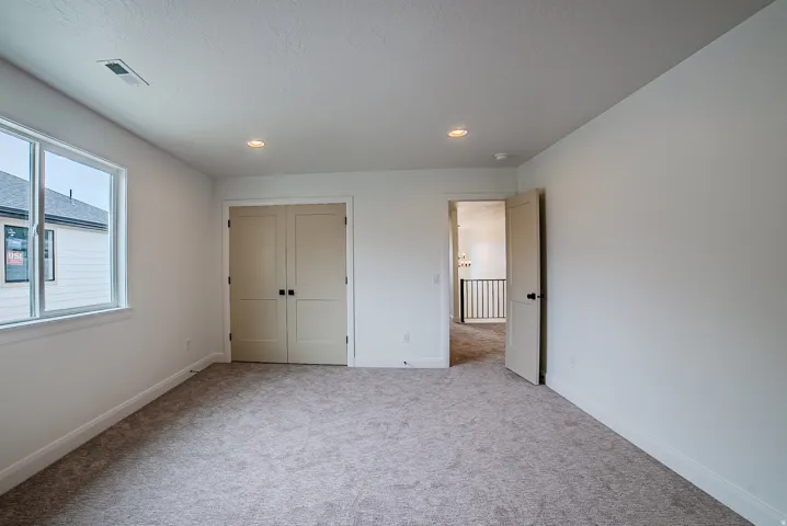 Carpeted room featuring a large window, double closet doors, recessed lighting, and white baseboards
