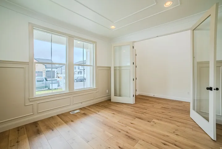 Room featuring wood-finish flooring, wainscoting details, and a coffered ceiling with recessed lighting