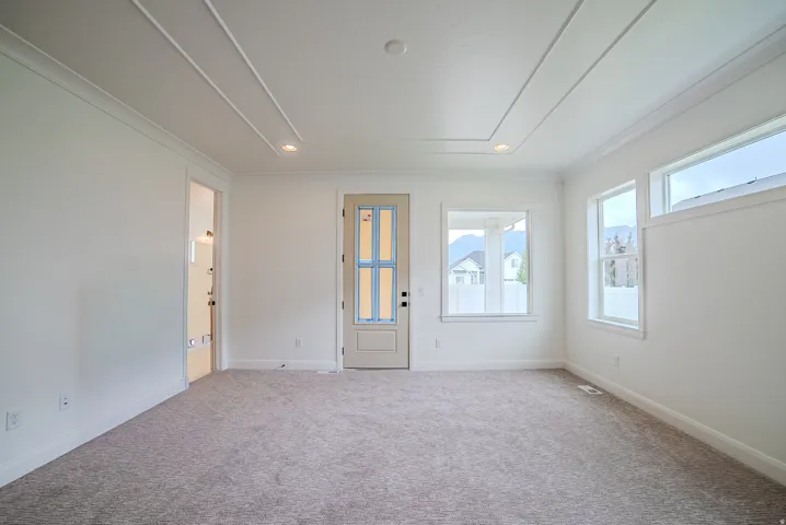 Spacious room featuring neutral carpeting, a tray ceiling with recessed lighting, and multiple windows providing ample natural light