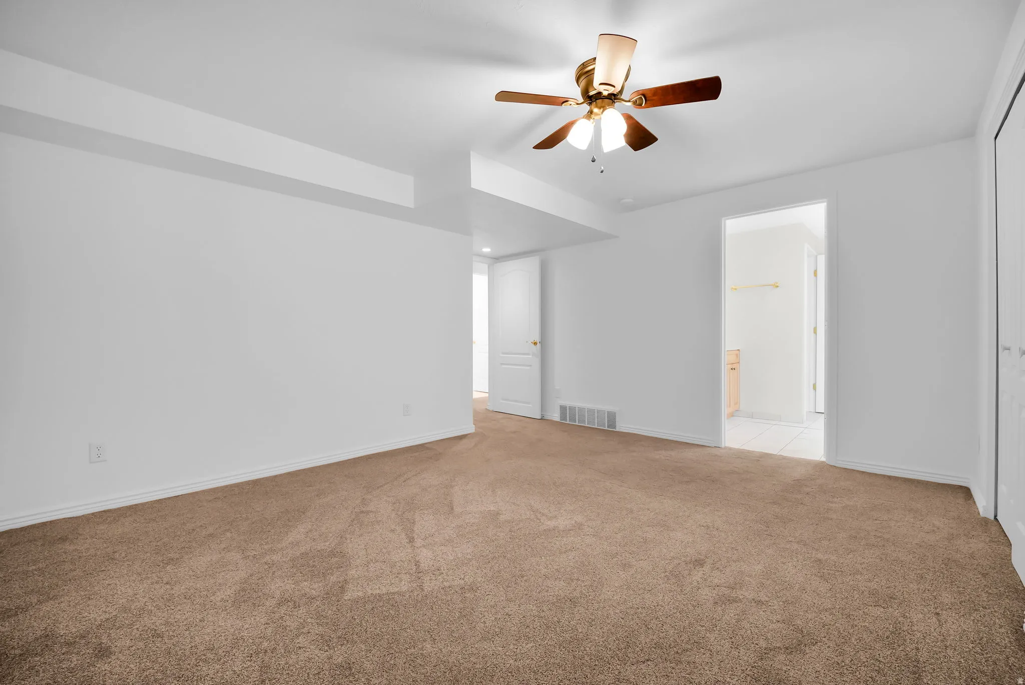 Spacious room featuring neutral carpeting, white walls, and a ceiling fan with integrated lighting