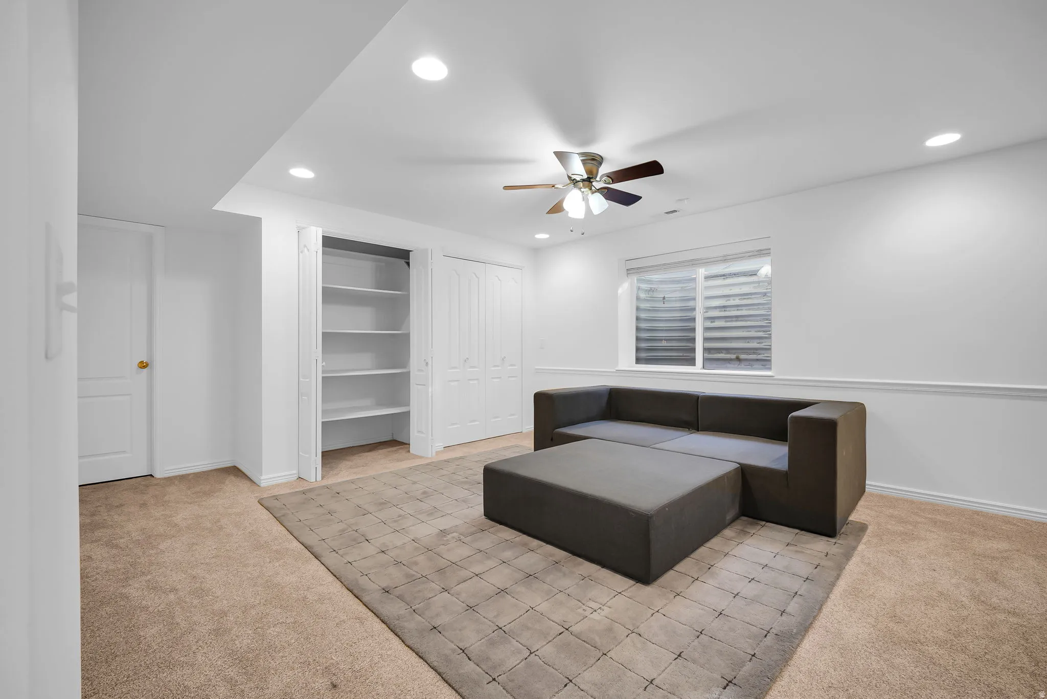 Spacious carpeted room featuring a ceiling fan, recessed lighting, and a window with blinds