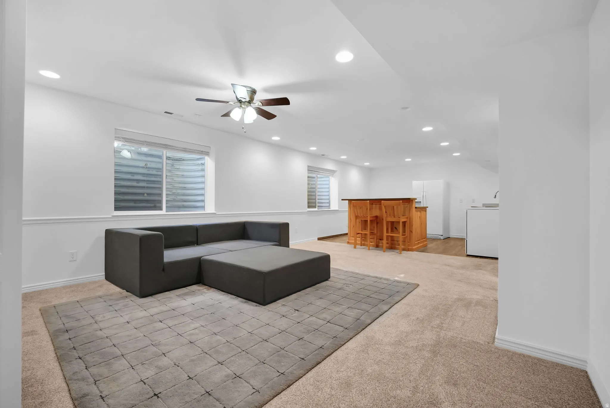 Spacious lower-level area with recessed lighting, ceiling fan, carpet flooring, and two egress windows