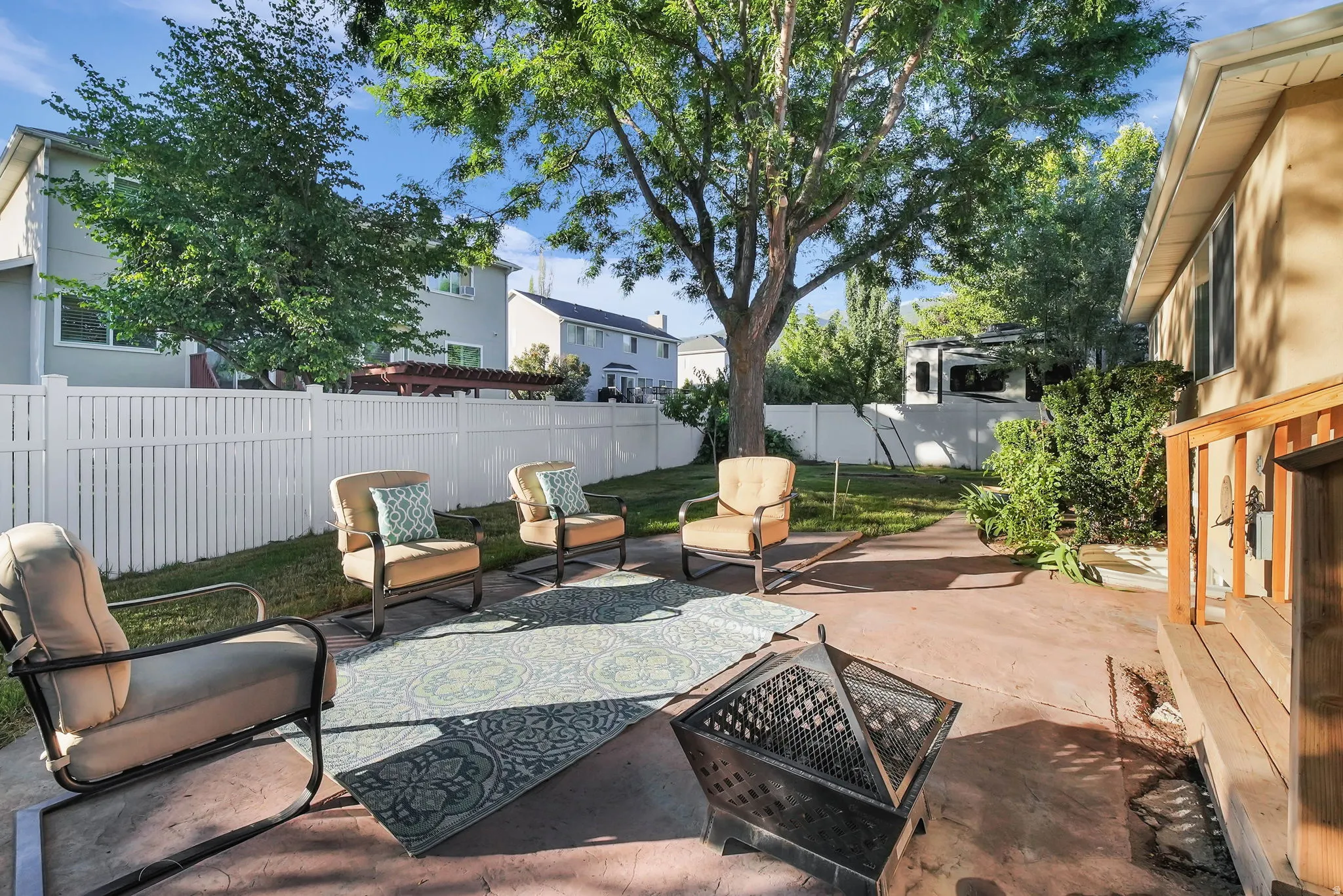Expansive backyard featuring a concrete patio, mature trees, and a white privacy fence