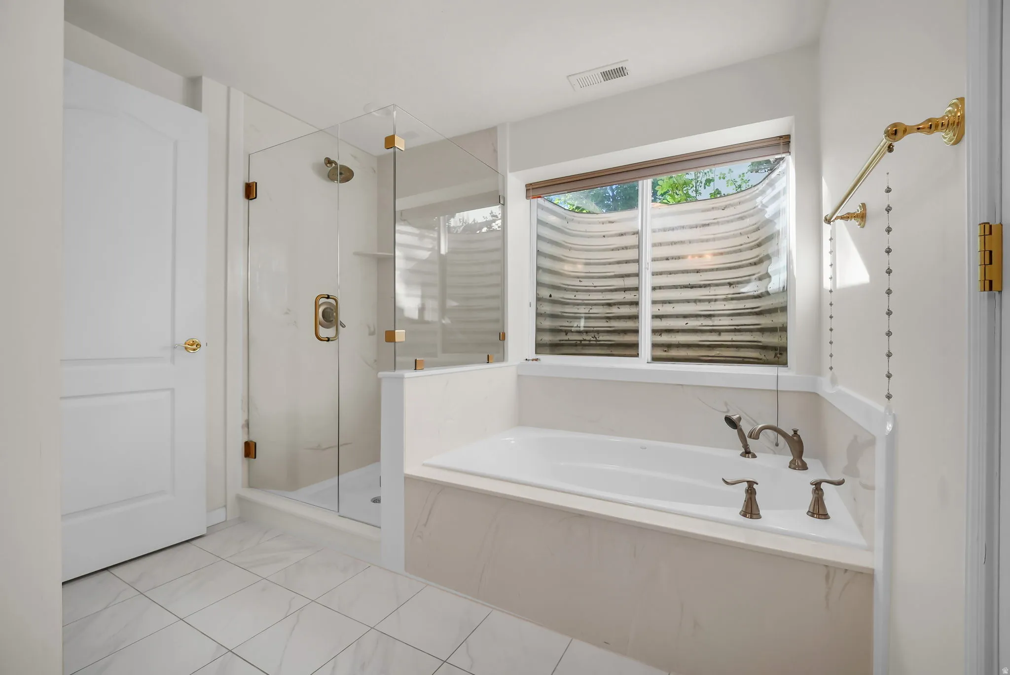 Bathroom featuring a built-in soaking tub with a window, a glass-enclosed shower, white tile flooring, and a white paneled door