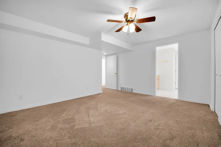 Spacious room featuring neutral carpeting, white walls, and a ceiling fan with integrated lighting