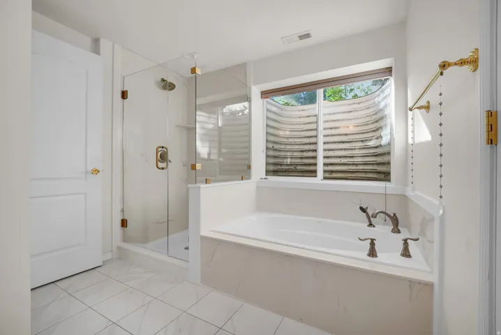Bathroom featuring a built-in soaking tub with a window, a glass-enclosed shower, white tile flooring, and a white paneled door