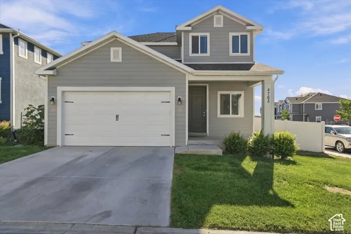 Gray siding exterior with white trim, a covered porch, an attached garage, a concrete driveway, and a small front lawn