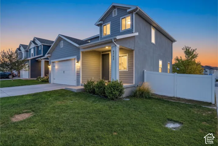 Two-story residence featuring a covered front porch, attached garage, and a white privacy fence