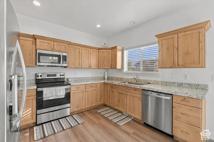 Kitchen featuring natural wood-finish cabinetry, light-toned countertops, stainless steel appliances, and wood-finish flooring