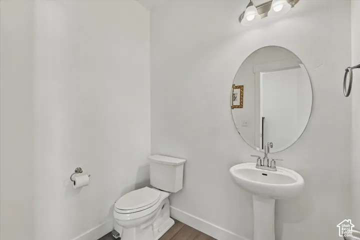 Pedestal sink with chrome faucet, oval mirror, and wood-finish flooring