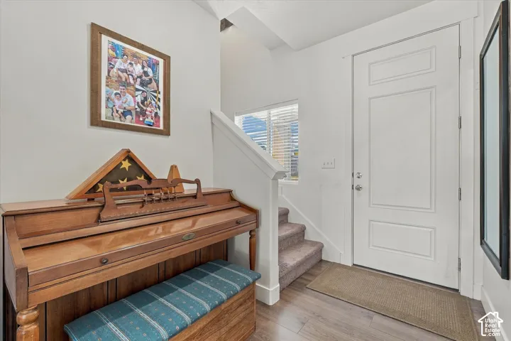 Wood-finish flooring, white paneled door, carpeted staircase, and window with blinds