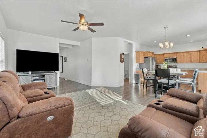 Open-concept living area with wood-finish flooring, a ceiling fan with integrated lighting, and a dining area featuring a chandelier