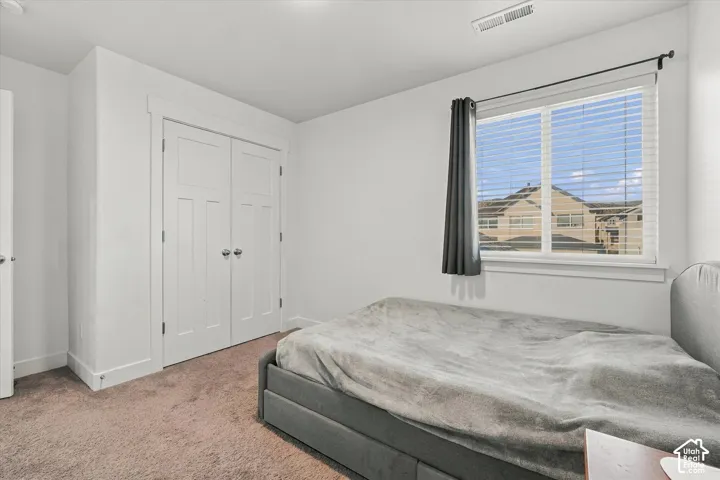 Carpeted room featuring a double-pane window with blinds, white trim, and a double-door closet with polished hardware