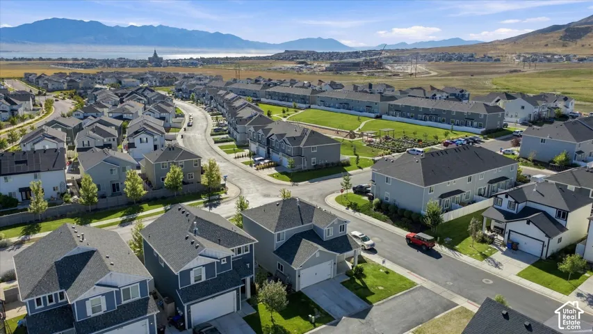 Modern residential development featuring single-family homes and townhomes, a community green space, and distant mountainous terrain