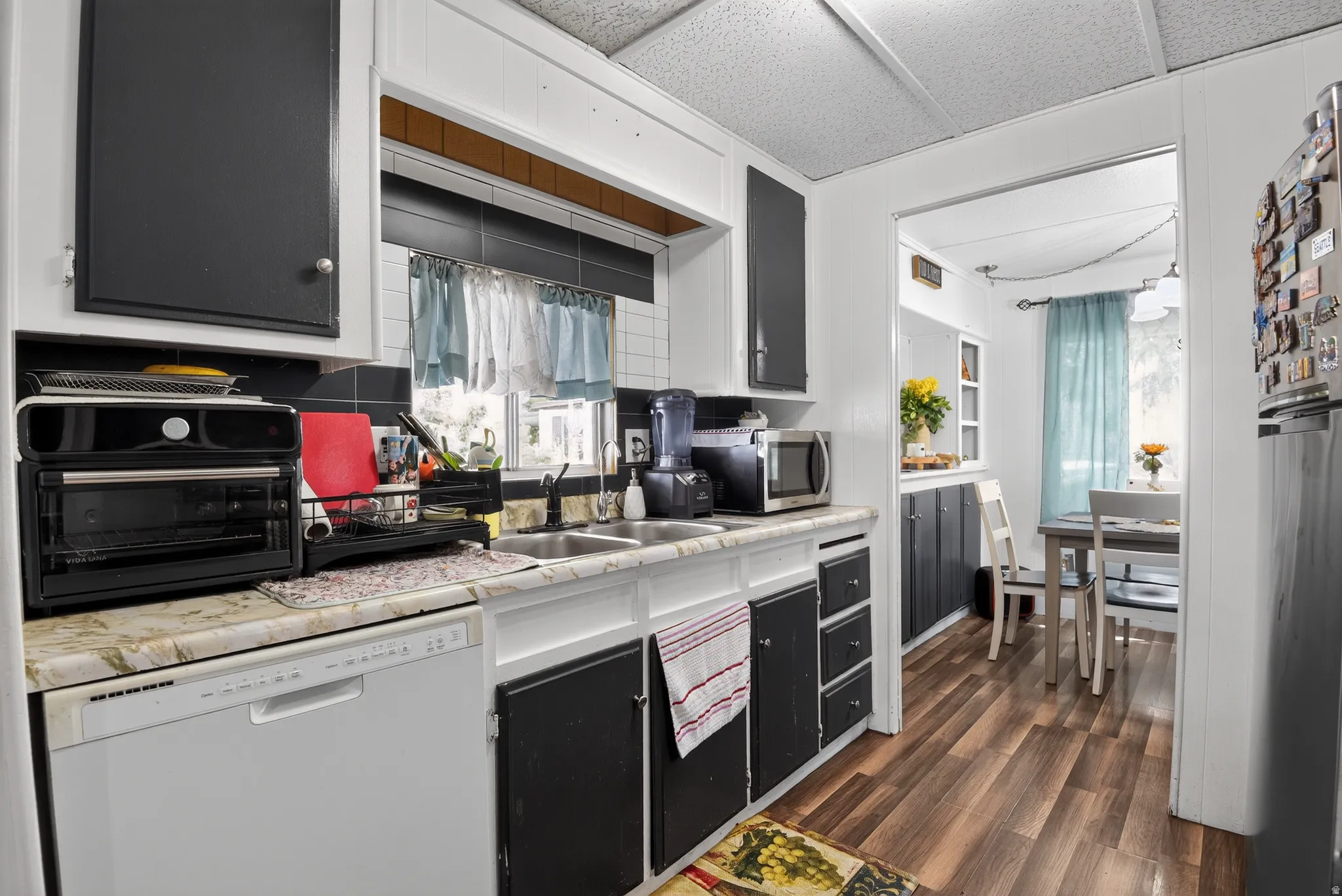 Kitchen featuring black and white cabinetry, a double basin sink, a white built-in dishwasher, and wood-finish flooring