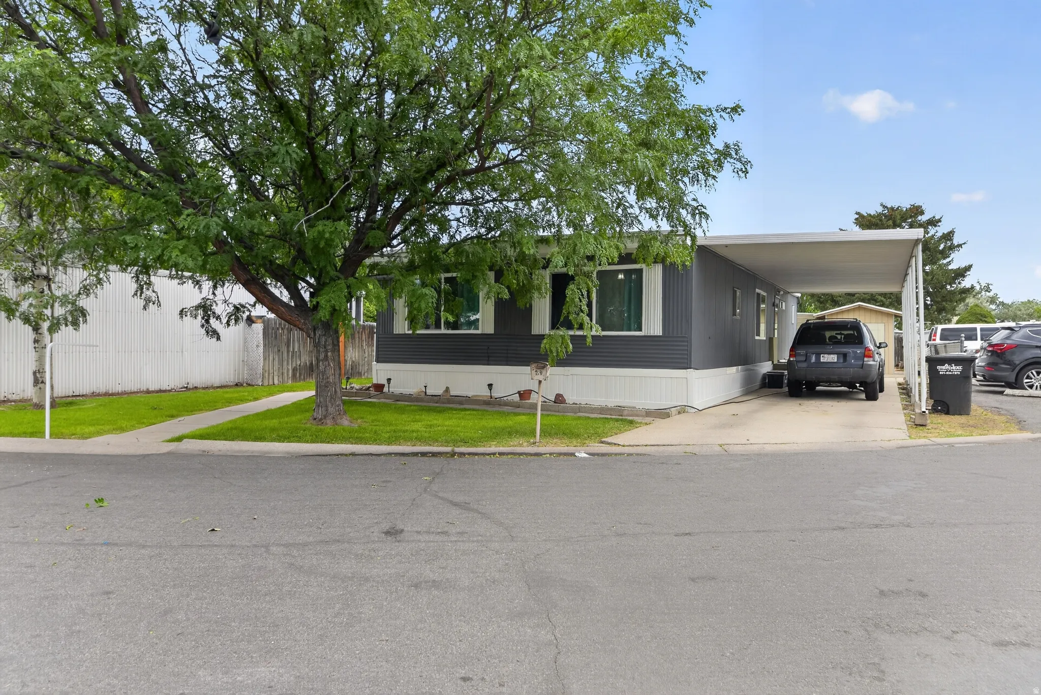 Single-story residence featuring gray siding with white trim, a covered carport, and mature trees