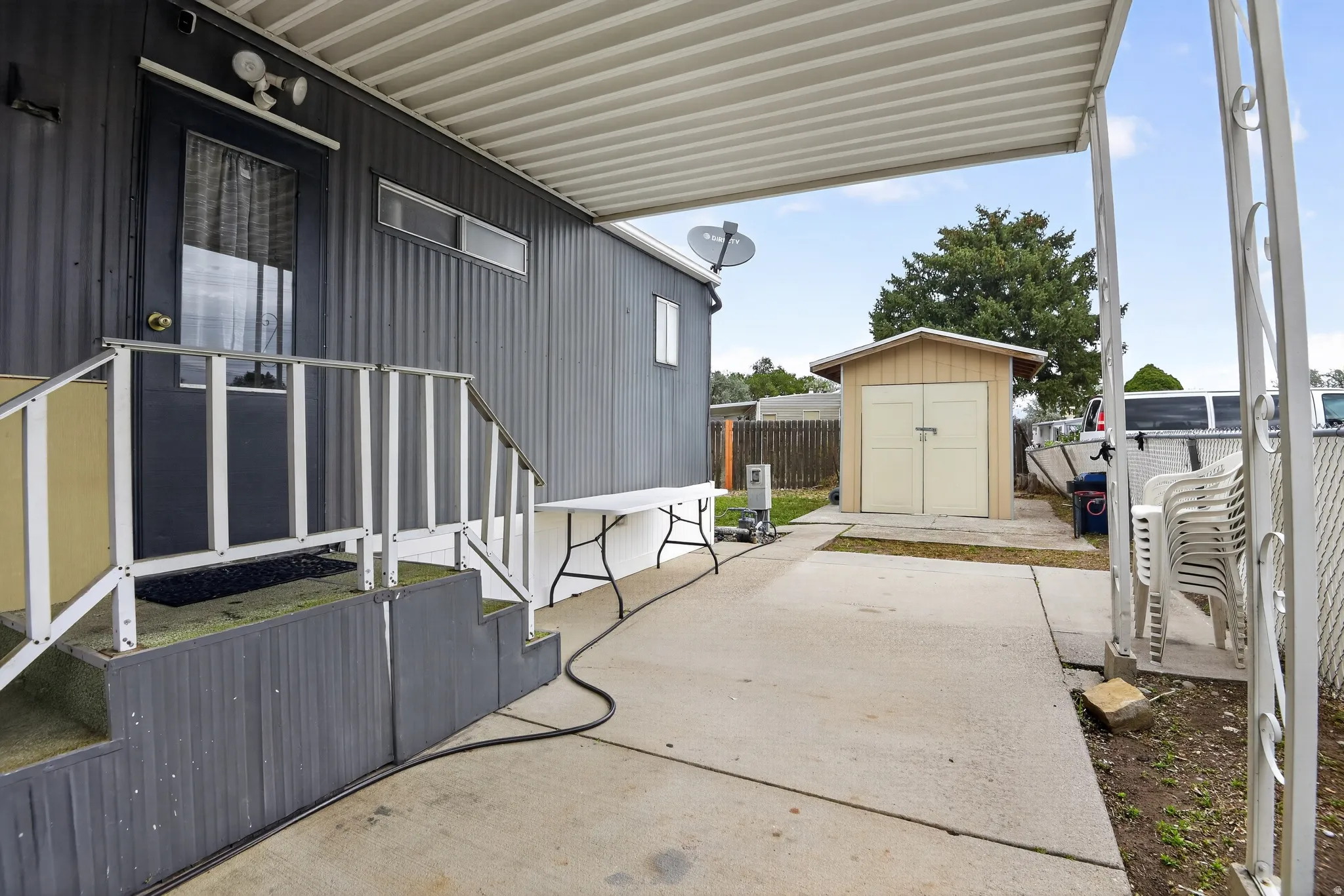 Exterior featuring corrugated siding, covered patio area, concrete patio, exterior steps with handrails, and a detached storage shed