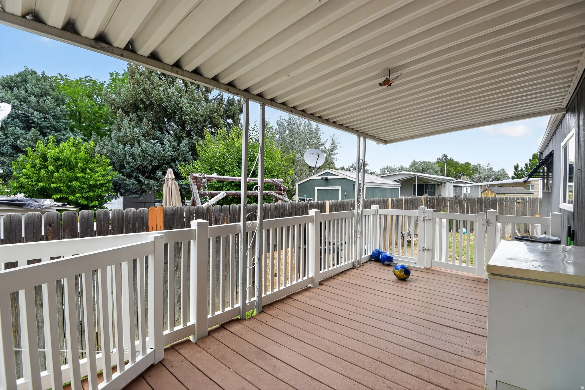 Covered wood-finish deck featuring white railings and a white gate