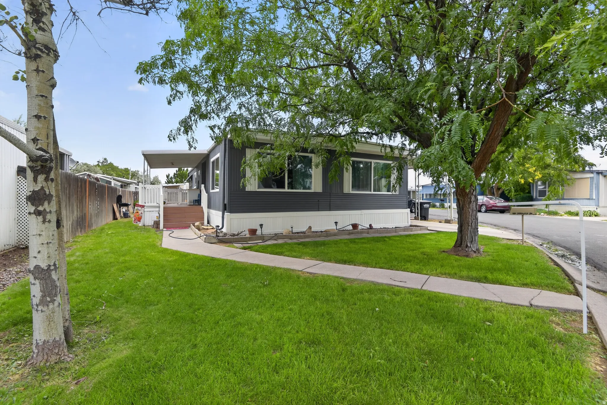 Manufactured home featuring dark gray siding with white trim, a covered porch, and mature trees