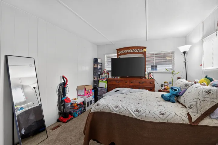 Bedroom featuring white paneled walls, carpet flooring, and white window blinds