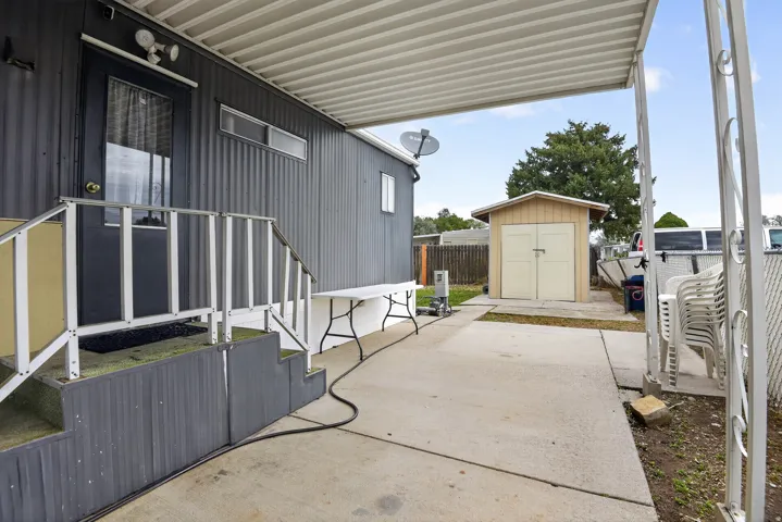 Exterior featuring corrugated siding, covered patio area, concrete patio, exterior steps with handrails, and a detached storage shed