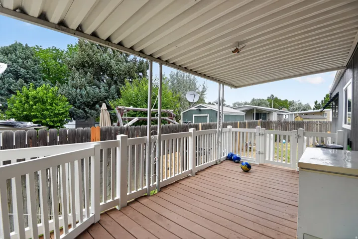 Covered wood-finish deck featuring white railings and a white gate