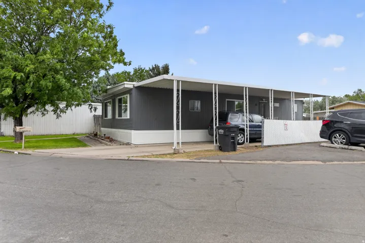 Exterior featuring gray siding with white trim, a covered carport, and a white privacy fence
