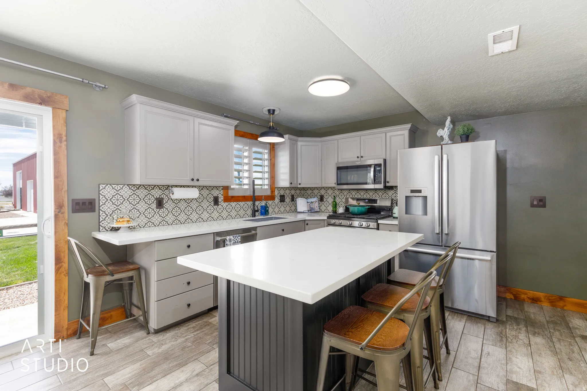 Kitchen featuring light gray cabinetry, stainless steel appliances, a patterned tile backsplash, tile flooring, and a central island with a white countertop