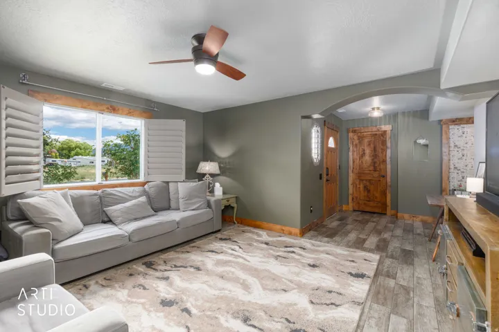 Spacious living area featuring a large window with plantation shutters, tile flooring, and a ceiling fan