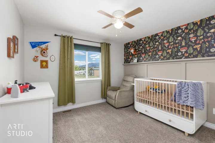 Carpeted bedroom featuring a wood-finish ceiling fan, a window with mountain and sky scenery, and a decorative accent wall with paneling