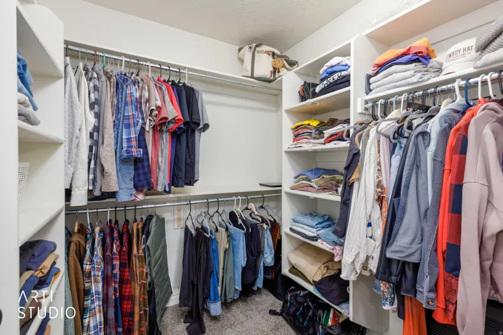 Walk-in closet featuring white built-in shelving, multiple hanging rods, and light gray carpeting
