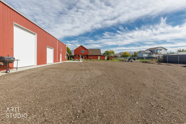 Expansive gravel lot with a red metal building featuring two large roll-up doors and a pedestrian door