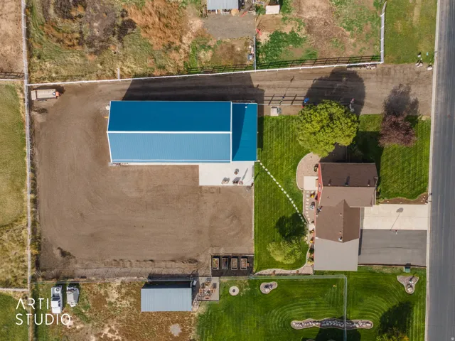 Aerial property overview featuring a large blue-roofed outbuilding, a red-sided residence with a brown shingle roof, and a substantial uncultivated land area