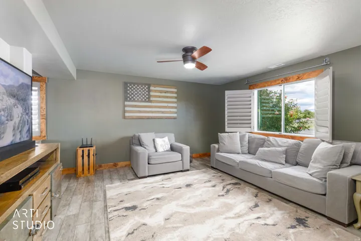 Spacious living area featuring tile flooring, a ceiling fan with integrated lighting, and a large window with plantation shutters