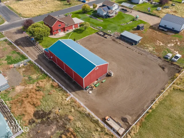Spacious property featuring a large red barn with a blue metal roof, a red residential structure with a shingled roof, a substantial fenced lot