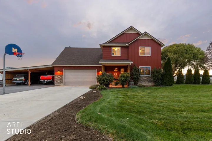 Red siding residence featuring a covered front porch, an attached garage, a multi-car carport, a concrete driveway, and a manicured lawn