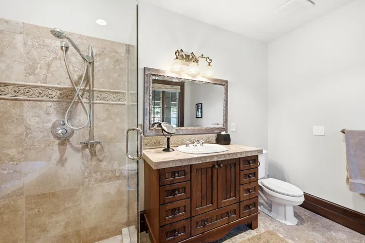 Glass-enclosed shower with stone tile surround and decorative accent band, featuring a handheld showerhead
