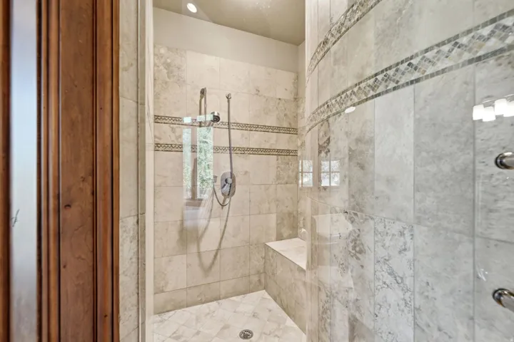 Walk-in shower featuring light-toned tile, a decorative mosaic tile band, a built-in bench, and a dual shower head system