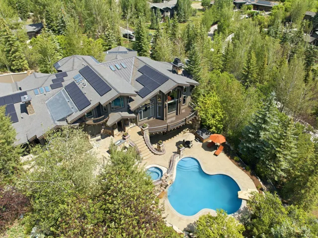 Contemporary residence featuring a multi-level roofline with integrated solar panels, an expansive outdoor patio, a freeform swimming pool, and an in-ground spa, all surrounded by dense mature trees