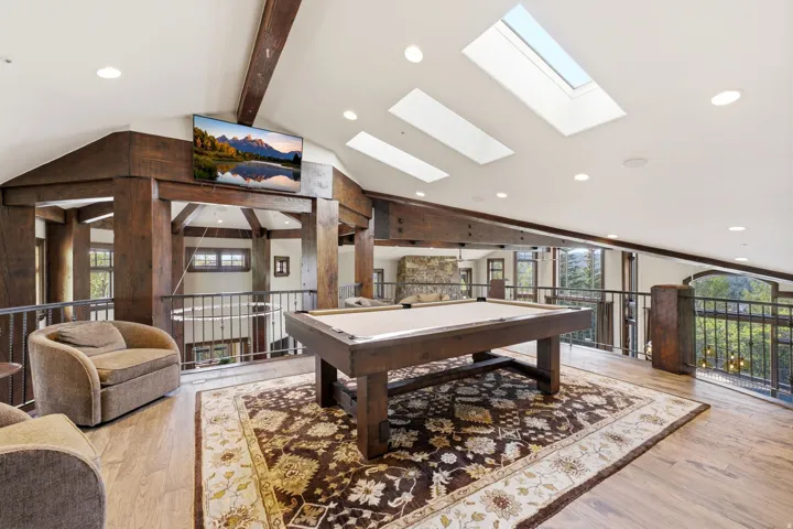 Spacious loft area featuring a billiard table, wood-finish flooring, and exposed timber beams
