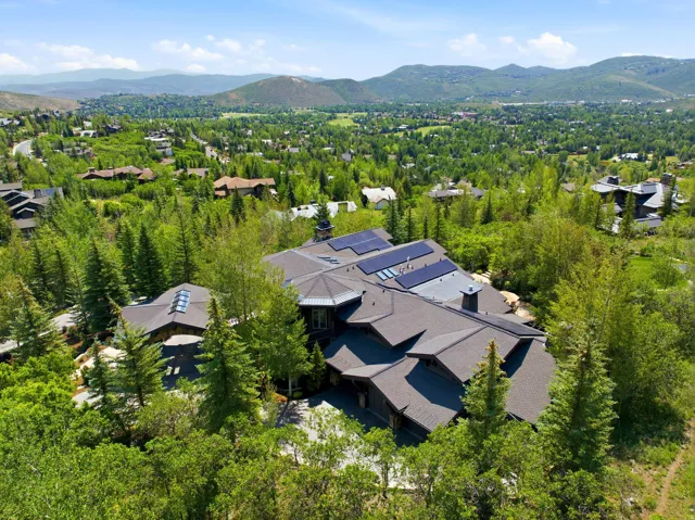 Expansive property with a multi-level roofline and numerous solar panels, surrounded by mature trees