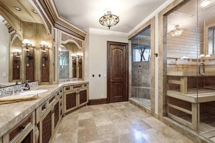 Spa-inspired bathroom featuring a glass-enclosed sauna, glass-enclosed shower with tile surround, and a double vanity with integrated sinks