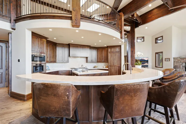 Gourmet kitchen featuring a curved island with stone countertop, wood cabinetry, stainless steel double oven, and wood-finish flooring
