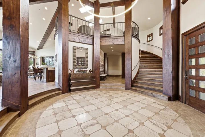 Grand foyer featuring a circular tiled floor inlay, exposed wood beams, a curving staircase with a wrought iron railing, a wood entry door with frosted glass panels, and recessed ceiling lighting