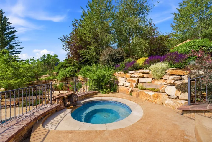 Outdoor spa with surrounding hardscaping, a stone retaining wall, and diverse plantings