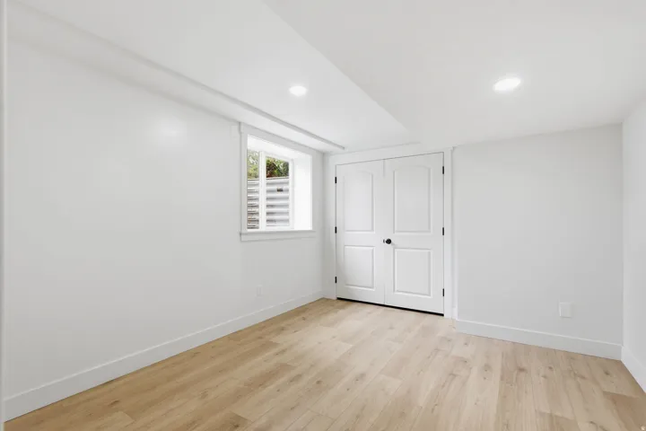 Room featuring light wood-finish flooring, recessed ceiling lighting, a window with a white frame, and a pair of double panel doors with matte black hardware
