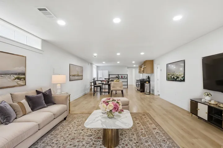 Open-concept living area with light wood-finish flooring, recessed ceiling lighting, and a kitchen area featuring wood cabinetry